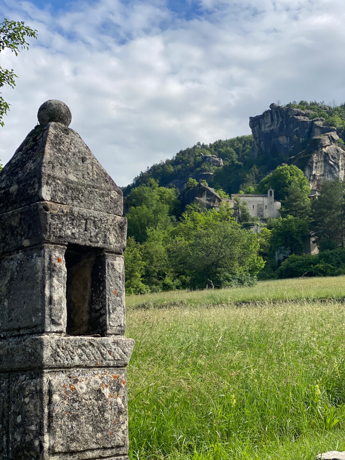 Oratoire de pierre au premier plan, la chapelle Notre-Dame de Vers-la-Ville visible au loin dans les rochers