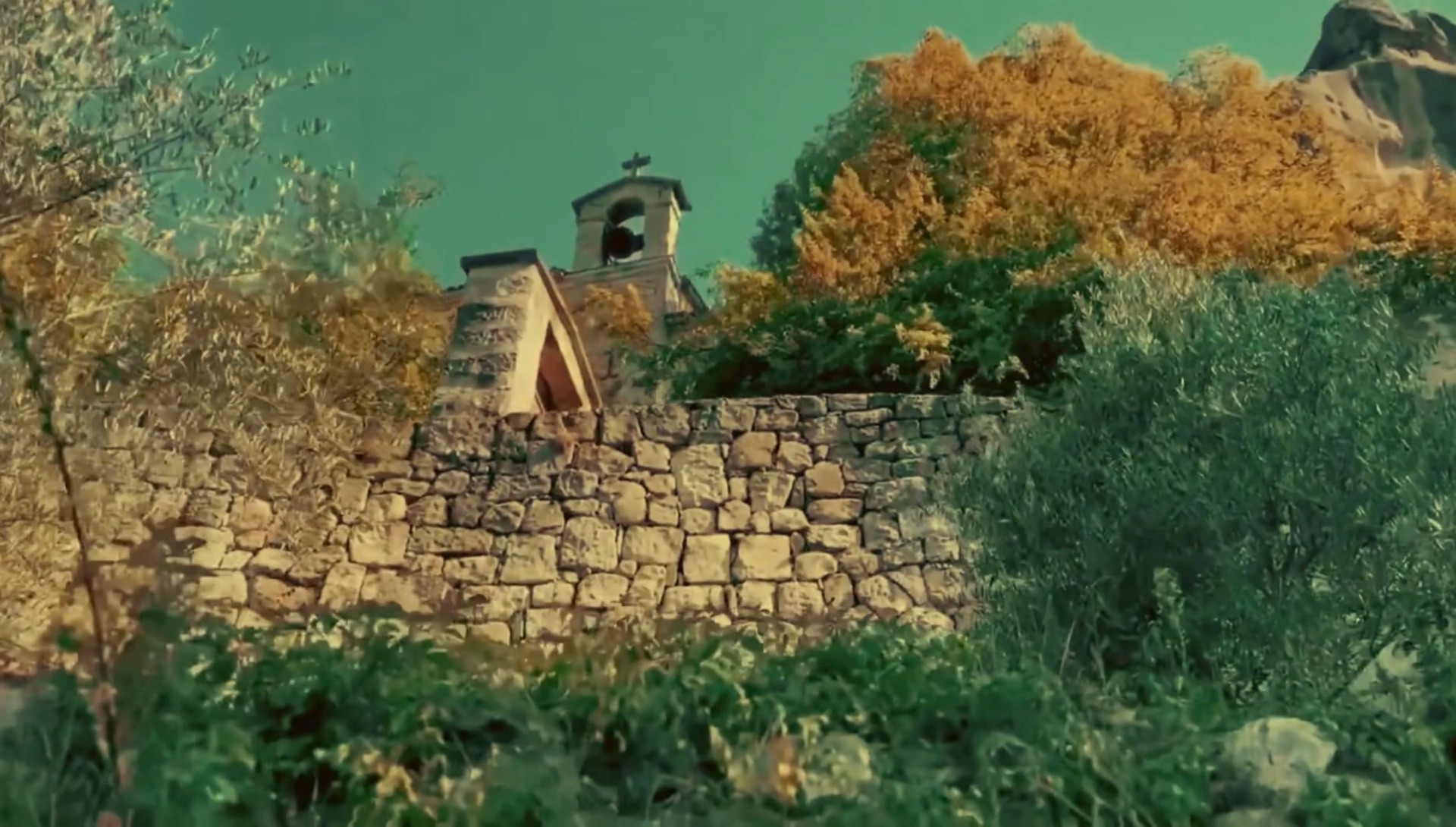 La chapelle Notre-Dame de Vers-la-Ville et son clocheton, derrière un mur en pierres sèches, au milieu de la végétation et des grès d'Annot