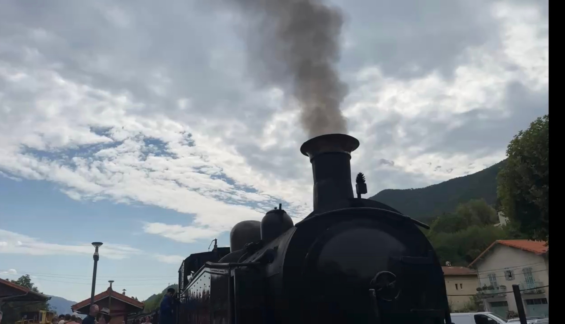 Le train à vapeur en gare, entouré de voyageurs, au pied des montagnes