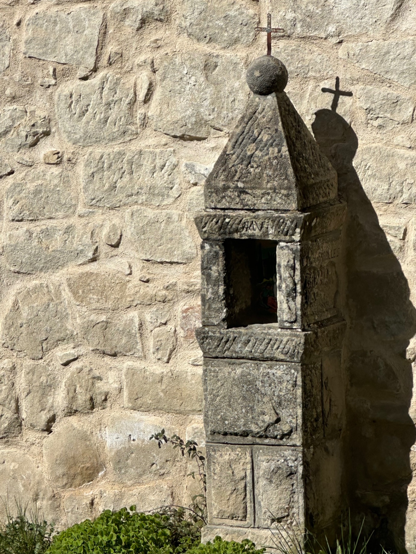 Oratoire de pierre sculpté surmonté d'une boule et d'une croix de fer, adossé au mur de la chapelle