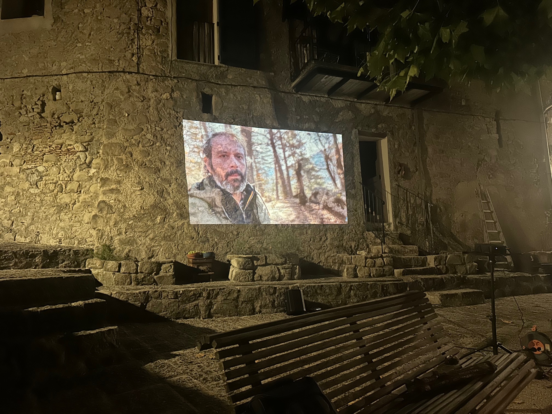 Projection sur la façade en pierre : le colporteur sous les pins de Haute-Provence.